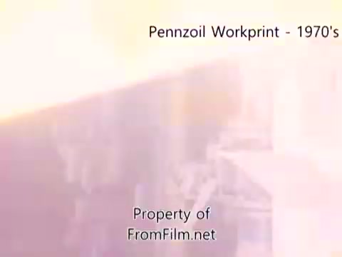The still from the 'Pennzoil Factory/Refinery Workprint - 1980s' shows a scene likely depicting operations within a Pennzoil refinery. The image has a softer focus and may exhibit some light leaks or color shifts, typical of 16mm film. There is visible debris in the film gate, enhancing the vintage feel. The accompanying music by Underbelly adds an atmospheric layer, complementing the industrial visuals.
