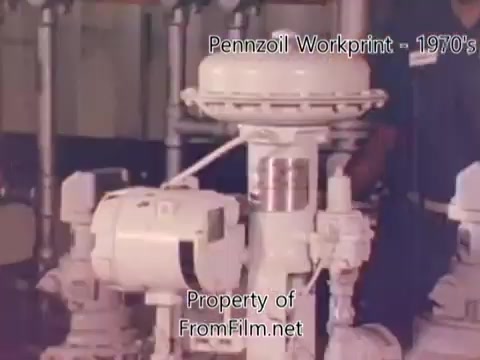 The still from the 'Pennzoil Factory/Refinery Workprint - 1980's' features industrial equipment, likely part of the refinery's machinery. The visible element is a control panel or valve mechanism, indicative of the technology used in the oil refining process. The film, shot on 16mm, may show some debris in the gate, which adds to its vintage quality. The accompanying music from Underbelly sets a reflective atmosphere, enhancing the observational nature of the footage.