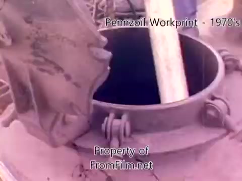 The still from the 'Pennzoil Factory/Refinery Workprint - 1980s' features an industrial scene with a large metal vessel, possibly a tank or reactor. The lid is slightly opened, revealing the interior, which seems to contain some material or substance. The image has a vintage look typical of 16mm film, with some visible debris in the film gate, indicative of its age and the medium used. The workprint context suggests it may document refinery operations or processes. The accompanying music from Underbelly enhances the atmospheric feel of the footage.