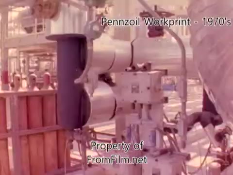 The still from 'Pennzoil Factory⧸Refinery Workprint - 1980's' features industrial machinery and equipment, showcasing the inner workings of the Pennzoil refinery. The scene captures the complexity of the refinery operations, with various pipes and machines in view. There's a noticeable film grain, and some debris appears in the film gate at certain points, indicating wear or age. The accompanying music by Underbelly adds to the atmospheric tone of the footage.