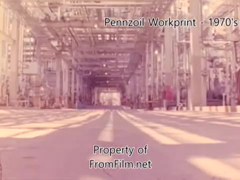 The still appears to show an expansive view inside a Pennzoil refinery from the 1970s, captured on 16mm film. The scene includes industrial structures, pipelines, and equipment, highlighting the scale and complexity of the facility. Debris is visible in the film gate, indicating some wear from the film's age. The accompanying music by Underbelly suggests a reflective or atmospheric tone, enhancing the industrial context of the imagery.