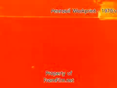The still from the 'Pennzoil Factory⧸Refinery Workprint - 1980's' shows a vibrant orange tint, characteristic of older 16mm film stock. The image is likely heavily affected by age, with visible debris in the film gate, indicating wear and tear. The workprint captures the industrial essence of a refinery, exemplified by its raw visual aesthetic. The accompanying music by Underbelly, featuring tracks like 'I Hear Voices' and 'Land's End,' adds an atmospheric layer to the presentation.