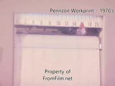 The still is from a 16mm workprint of the Pennzoil refinery, likely capturing the technical aspects of the film. It shows a ruler alongside the film strip, highlighting the measurement detail. The image might exhibit some debris in the film gate, which is common in older prints. The associated music tracks from Underbelly enhance the visual content with an atmospheric backdrop. Overall, it reflects a documentary style focused on industrial processes from the 1980s.