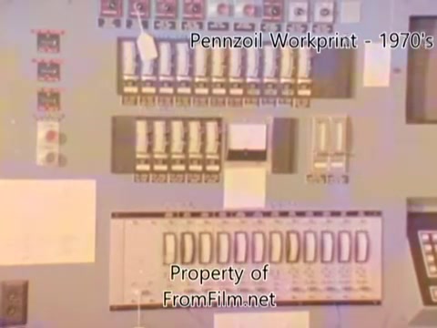The still from the 'Pennzoil Factory⧸Refinery Workprint - 1980's' shows a control panel with various switches, indicators, and dials, indicative of industrial machinery used in a refinery setting. The overall color palette appears slightly muted, characteristic of 16mm film from that era. The presence of debris in the film gate suggests some wear and tear typical of older film prints. The music from Underbelly adds an ambient atmosphere to the visual, creating a reflective mood associated with industrial environments.