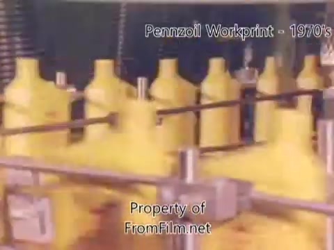 The still from the 'Pennzoil Factory⧸Refinery Workprint - 1980's' features a production line with several yellow oil containers in motion, likely depicting the bottling process at the Pennzoil refinery. The image suggests a busy industrial setting, characteristic of the film's era. Additionally, some debris is noted in the film gate, affecting the visual quality. Background music from Underbelly enhances the atmosphere, contributing to the overall vibe of the workprint.