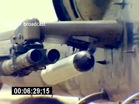 The still from the 'USMC Aviation Ordnance Recruiting Film' shows a close-up of weaponry attached to a military aircraft. Prominent features include dual barrel structures, likely rocket or missile launchers, and a cylindrical ordnance piece. The focus emphasizes the aircraft's armament capabilities, underscoring the role of aviation ordnance in the Marine Corps. The image captures a moment of military readiness, showcasing advanced technology.