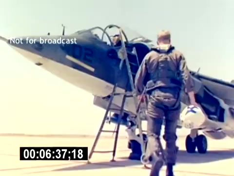 The still from the 'USMC Aviation Ordnance Recruiting Film - Silent' features a military aircraft, presumably a fighter jet, on an airstrip. A service member in aviation gear is climbing up a ladder to enter the aircraft, while another individual is already seated inside. The scene highlights the process of preparing for flight, emphasizing the operational aspect of marine aviation and ordnance. The bright daylight and military setting suggest an active airfield environment.
