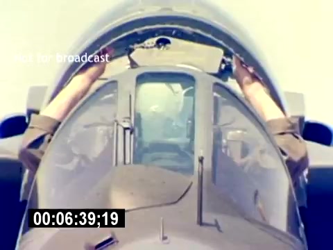 The still from the 'USMC Aviation Ordnance Recruiting Film - Silent' shows a close-up view of a military aircraft cockpit. The focus is on a pilot's hands, which are engaged in operating or adjusting the cockpit controls. The front canopy is visible, along with the cockpit structure, conveying a sense of precision and technical proficiency associated with aviation ordnance roles in the Marine Corps. The overall context emphasizes the skills and responsibilities required in the field of aviation within the military.