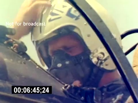 The still from the 'USMC Aviation Ordnance Recruiting Film' shows a pilot inside a cockpit, adjusting their helmet. They are wearing a mask that covers part of their face, suggesting preparation for a flight. The atmosphere appears focused and serious, emblematic of the military's aviation environment. A timestamp on the bottom indicates the film's duration, and there's a watermark stating 'Not for broadcast.'