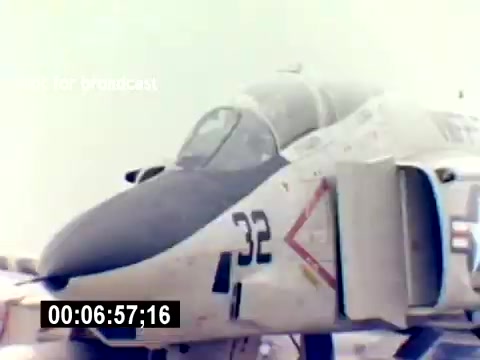 The still depicts a military aircraft, specifically a fighter jet, with the number “32” visible on its side. The aircraft features a distinctive color scheme, likely indicative of its service branch. The image captures the jet in a bright, outdoor setting, emphasizing its design and potential operational capabilities. The overall context suggests it is part of a recruitment film aimed at illustrating the advanced technology and prowess of the USMC Aviation Ordnance.