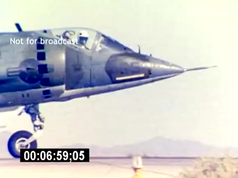 The 16mm still from the 'USMC Aviation Ordnance Recruiting Film - Silent' features a close-up of a military aircraft, highlighting its nose and cockpit area. The aircraft appears to be on the ground, potentially during pre-flight preparations. The setting is likely a desert or military base, given the arid landscape in the background. The focus emphasizes the aircraft's design and capabilities, aligning with the recruiting theme of showcasing USMC aviation technology. The image is marked with 'Not for broadcast' and includes a time code.