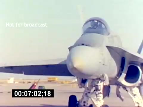 The 16mm still depicts a close-up view of a military aircraft, likely a fighter jet, on a tarmac. The aircraft's nose is prominent, showcasing its sleek design and cockpit. The background reveals airfield infrastructure, hinting at an operational military environment. It includes a timecode, and a watermark indicating it’s not for broadcast, suggesting this is a behind-the-scenes or training film from the USMC Aviation Ordnance Recruit Film series. The lack of sound reinforces its silent film status.