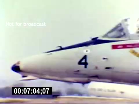 The still features the close-up of a military aircraft, specifically focusing on the nose and cockpit area. The aircraft is labeled with the number '4' and appears to be part of a USMC (United States Marine Corps) context, indicative of aviation ordnance. The background suggests an airfield setting, likely during a recruitment film highlighting military aviation. The image is noted as not for broadcast, indicating it's intended for limited viewing or archival purposes.