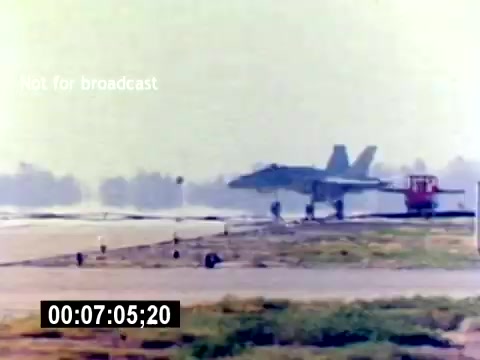 The still from the 'USMC Aviation Ordnance Recruiting Film' shows a military jet, likely an F/A-18, taking off from an airstrip. In the foreground, ground personnel and equipment are visible, implying active operations at a military base. The scene is characterized by a clear sky and vibrant colors, highlighting the aircraft's departure. The timestamp at the bottom suggests the moment is captured at 7 minutes and 5 seconds into the film. The overlay indicates that the footage is not for broadcast.