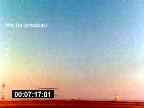 The still from the 'USMC Aviation Ordnance Recruiting Film - Silent' features a vast, clear sky transitioning from blue to orange near the horizon, indicating either dawn or dusk. In the foreground, there is minimal landscape, suggesting an airfield or open area, with basic structures visible, possibly connected to aviation operations. The frame includes a timestamp at the bottom and a label indicating it is not for broadcast. The overall atmosphere conveys a sense of calm and readiness, typical of military training visuals.