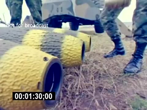 The still from the 'USMC Aviation Ordnance Recruiting Film - Silent' shows military personnel handling ordnance, specifically focusing on munitions with a yellow and black design. Soldiers are positioned on the ground, possibly preparing the equipment for deployment or inspection. The scene emphasizes military training and the technical aspects of aviation ordnance, highlighting the importance of safety and precision in handling such materials. The setting appears to be outdoors, likely on a training field.