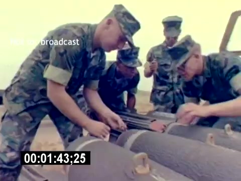 The still from the 'USMC Aviation Ordnance Recruiting Film - Silent' shows several uniformed Marines working together on military ordinance. They are focused on handling or inspecting what appears to be munitions. The scene highlights teamwork and technical expertise in a training or operational environment. The background suggests an outdoor setting, likely on a military base or training ground.