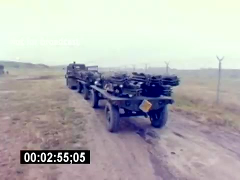 The still from the 'USMC Aviation Ordnance Recruiting Film - Silent' depicts a military vehicle transporting what appear to be munitions or ordnance. The scene is set in an open, likely rural area, with a cloudy sky suggesting overcast weather. The vehicle is shown on a dirt road, indicating an operational military environment, while a fence is visible in the background, hinting at a secured facility or area. The timestamp at the bottom suggests the footage is part of a larger film sequence.