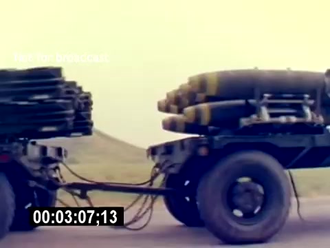 This still from the 'USMC Aviation Ordnance Recruiting Film - Silent' shows a military vehicle transporting ordnance. The vehicle is equipped with multiple munitions mounted on its flatbed, highlighting the logistics involved in aviation ordnance. The setting appears to be open terrain, emphasizing military operations. The timestamp indicates a moment in the sequence of the film.