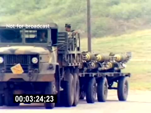 The still from the 'USMC Aviation Ordnance Recruiting Film - Silent' depicts a military flatbed truck, camouflaged and loaded with ordnance, likely munitions or missiles. The truck is positioned on a roadway, with a military personnel visible in the cab. The background features grassy terrain, typical of a training or operational environment. The image is marked 'Not for broadcast' and includes a timestamp.