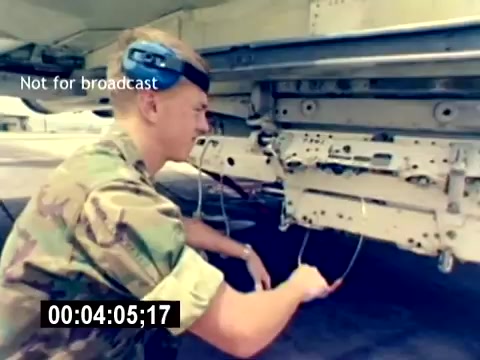 The 16mm still from the 'USMC Aviation Ordnance Recruiting Film - Silent' depicts a U.S. Marine in military camouflage working on the underside of an aircraft. He is focused on connecting or disconnecting wires from the aircraft’s ordnance system, demonstrating hands-on technical skills relevant to aviation ordnance. The scene emphasizes the practical aspect of the role, showcasing the Marine's competence in maintaining equipment crucial for military operations. The clip is marked “Not for broadcast” and includes a timecode indicating the duration at a specific moment in the film.