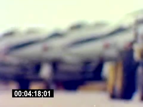 The still from the 'USMC Aviation Ordnance Recruiting Film - Silent' depicts a blurred view of several military aircraft lined up. The focus appears soft, suggesting either a camera movement or a focus issue. The background features machinery or ground equipment, hinting at an aviation environment. The lack of sharp details adds a dreamlike quality to the image, drawing attention to the aircraft. Timecode at the bottom indicates the segment of the film.
