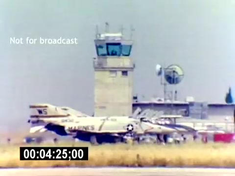 The still from the 'USMC Aviation Ordnance Recruiting Film' features two military aircraft on a runway in front of an air traffic control tower. The planes are marked with 'MARINES' and bear the designation 'WS,' indicating their connection to the U.S. Marine Corps. The background includes various antennas and equipment typical of an airfield, with a grassy area in the foreground. The timestamp indicates a moment in the film, and there's a 'Not for broadcast' notice overlaying the image.