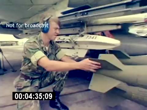 The still features a Marine in camouflage uniform and headphones, crouched next to a military aircraft. He appears to be handling an ordnance, likely preparing or inspecting a missile attached to the aircraft. The scene emphasizes the technical aspects of aviation ordnance operations within the US Marine Corps. A timestamp and the note 'Not for broadcast' indicate the film's archival nature.
