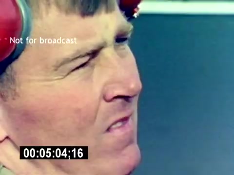 The still features a close-up of a male figure, likely a serviceman, wearing protective headphones. He appears focused or slightly tense, with a furrowed brow and pursed lips. The background is blurred, suggesting an outdoor or hangar environment. The timestamp at the bottom indicates the moment in the film, while the text above states it's not for broadcast. The overall tone suggests a serious or operational setting related to aviation ordnance.