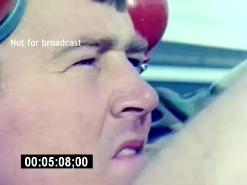 The still from the 'USMC Aviation Ordnance Recruiting Film - Silent' shows a close-up of a man, likely a Marine, focused and determined. He's wearing protective ear gear, suggesting he is involved in a technical or noisy environment. His expression reflects concentration, possibly indicating a moment of preparation or inspection related to aviation ordnance. The background is blurred, emphasizing his facial expression and gear.