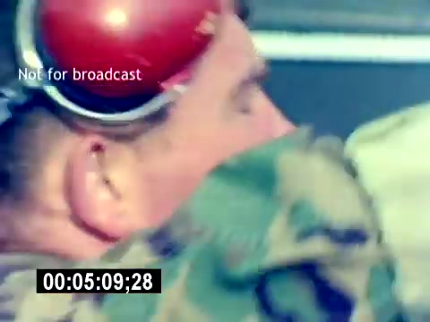 The still from the 'USMC Aviation Ordnance Recruiting Film - Silent' depicts a soldier wearing goggles and military camouflage. The focus seems to be on his profile, suggesting a attentive stance. There's a time stamp at the bottom, indicating the progression in the film (00:05:09:28), and a watermark stating 'Not for broadcast.' Overall, the image captures the essence of military life and training in aviation ordnance.