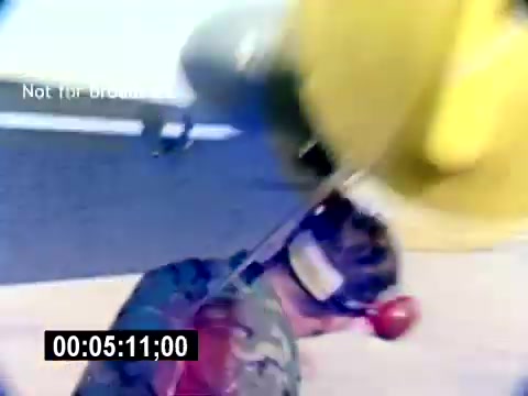 The still from the 'USMC Aviation Ordnance Recruiting Film - Silent' shows a serviceman in military camouflage working beneath an aircraft. He appears focused on his task, which may involve handling ordnance or equipment, highlighted by vivid colors from the aircraft's components above. The image captures the intensity and technical nature of aviation ordnance work.