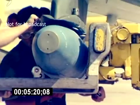 The still from the 'USMC Aviation Ordnance Recruiting Film - Silent' shows a close-up of a person attaching an ordnance item, possibly a bomb or missile, to an aircraft. The worker, dressed in a uniform, is focused on the task, which highlights the technical aspects of aviation ordnance handling. The background features parts of the aircraft and support structures, indicating a military aviation environment. The timestamp at the bottom suggests it's part of a longer sequence focused on U.S. Marine Corps aviation operations.