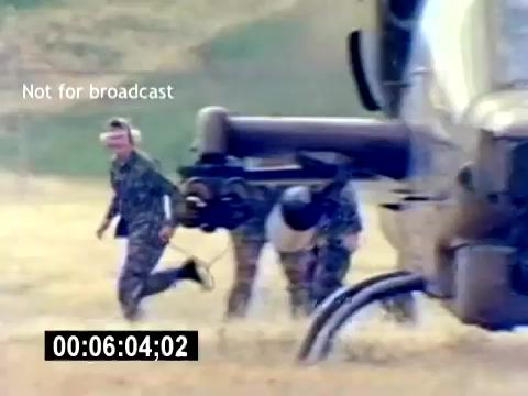 The still depicts a scene from the 'USMC Aviation Ordnance Recruiting Film,' showcasing military personnel engaged in an activity near a helicopter. A group of service members, dressed in camouflage uniforms, is seen running and working around the helicopter, possibly in a training or operational context. The image conveys a sense of urgency and teamwork, highlighting the role of aviation ordnance in the U.S. Marine Corps. The 'Not for broadcast' watermark indicates it's intended for internal or specific distribution only.