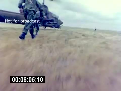 The still shows a scene from the 'USMC Aviation Ordnance Recruiting Film,' featuring military personnel in camouflage gear interacting with a helicopter, set against an open field and cloudy sky. The image conveys action and engagement, capturing the essence of aviation ordnance operations. A timestamp indicates the film’s position, with a 'Not for broadcast' label overlaying the scene.