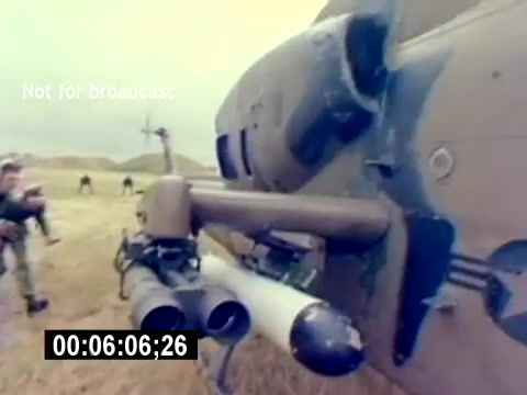 The still features a close-up view of a military helicopter, likely part of the USMC Aviation Ordnance. Visible are missile attachments under the helicopter's fuselage, with a focus on the ordnance setup. In the background, personnel appear to be preparing or observing the helicopter in an outdoor setting, likely during a training or recruiting scenario. The image conveys a sense of operational readiness and military engagement.