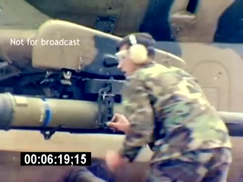 The still from the 'USMC Aviation Ordnance Recruiting Film - Silent' shows a Marine in camouflage uniform and ear protection working on munitions. He appears focused on attaching or adjusting a missile to a helicopter, highlighting the technical aspects of aviation ordnance. The scene emphasizes the hands-on, skilled nature of the role within the Marine Corps.