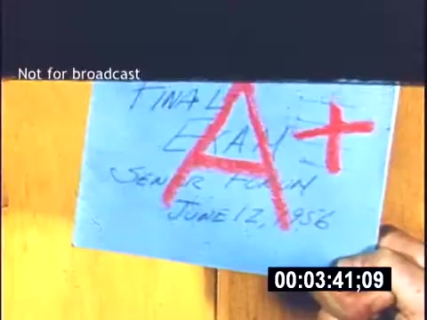 The still features a hand holding a blue sheet of paper with the text 'FINAL EXAM' written in a casual style, a large red 'A+' prominently displayed, and the date 'JUNE 12, 1956' noted. The background appears wooden, suggesting a simple, possibly home setting. A watermark indicates it is not for broadcast.