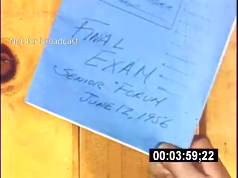 The still features a hand holding a blue folder marked 'FINAL EXAM' with the subtitle 'Senior Forum June 17, 1956.' The document appears to be part of a college context, likely associated with end-of-term assessments. The background is a wooden surface, suggesting a casual or personal setting. The time counter at the bottom indicates it is part of a video.