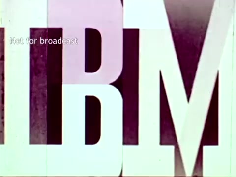 The still features a bold, stylized presentation of the IBM logo, incorporating a mix of block letters and varying shades. The text 'Not for broadcast' overlays the image, indicating that this material is for internal or limited sharing. The overall design is reflective of 1960s graphic design aesthetics, emphasizing technology and innovation. This captures the essence of IBM's role in modernizing educational administration through their computing solutions, which included punch cards for managing data.