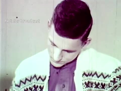 The still from 'IBM - The Information Center (1963)' features a young man wearing a patterned cardigan, focusing intently on a task, possibly related to the use of punch cards or data processing. This image illustrates the human interaction with emerging technology in education, emphasizing the applications of IBM's computing solutions for managing grades and course enrollment. The overall tone suggests a serious engagement with innovative software technology of the era.