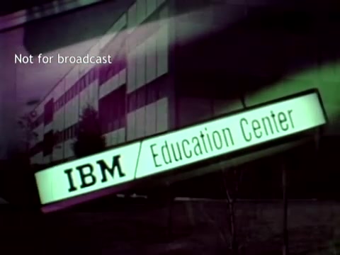 The still features an exterior view of an IBM Education Center, prominently displaying the IBM logo. The image indicates it's not for broadcast, suggesting it's intended for internal or archival use. The visual context relates to IBM’s educational initiatives and showcases the role of computer technology, particularly how it can streamline administrative tasks like managing grades and course enrollment using tools like punch cards. The overall aesthetic reflects 1960s technology and design.