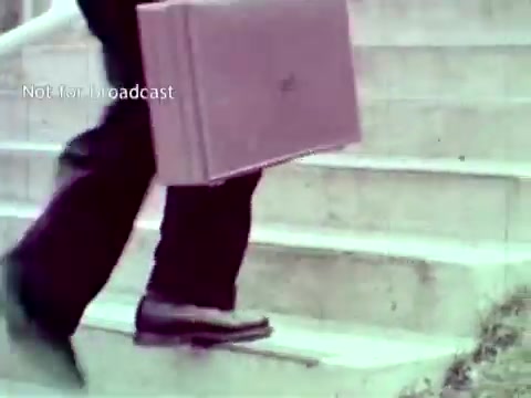 The still shows a person walking up a set of stairs while carrying a briefcase. The scene likely emphasizes the professional and educational context of the IBM technology being discussed. This visual aligns with the film's focus on the application of IBM's computer systems in managing educational functions, such as grades and course enrollment. The use of a briefcase suggests a formal environment, highlighting the integration of technology in educational administration.