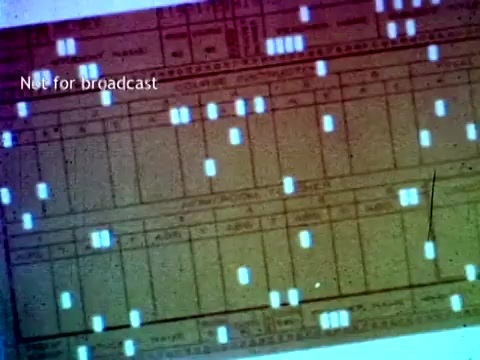 The still from 'IBM - The Information Center (1963)' features an overhead view of punched cards, which were used in early computing for data entry and processing. The cards display various rows and columns filled with holes, likely indicating grades or enrollment data. The vibrant colors suggest old film stock, while the text 'Not for broadcast' indicates its restricted use. This image reflects the technological capabilities of IBM at the time, highlighting their application in educational administration.