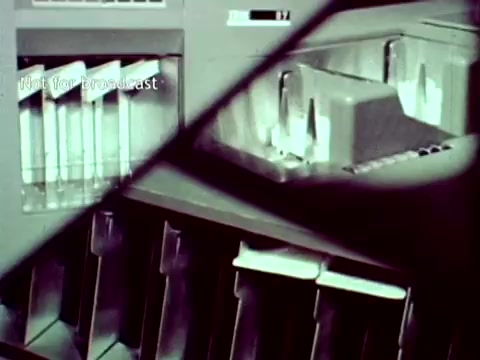 The still from 'IBM - The Information Center (1963)' features a close-up view of an IBM computer system, highlighting components such as punch card readers and storage units. The scene emphasizes the technological capabilities of IBM's systems during the era, particularly in managing educational data like grades and course enrollments. The image reflects the early integration of computing technology in administrative processes within education.