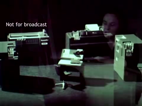 The still from 'IBM - The Information Center (1963)' showcases early IBM computing technology, featuring devices such as punch card machines. A woman is seen operating the equipment, emphasizing the integration of computing in educational administration tasks like managing grades and course enrollment. The visual highlights the technological advancements of the time and their application in enhancing educational processes.