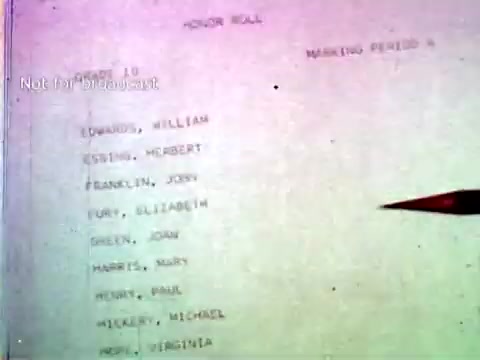 The still features a printed document labeled 'Honor Roll,' showing a list of names along with corresponding educational information, possibly grades or class periods. The document is being pointed to with a red pen, emphasizing the use of IBM technology for organizing academic data, reflecting the company's focus on educational applications in the 1960s. The image demonstrates the integration of computer technology, such as punch cards, in managing student records.