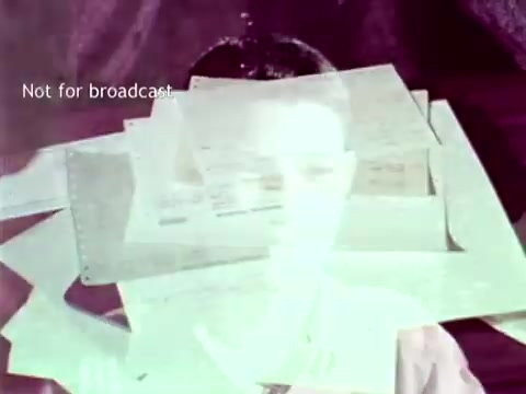 The still features a young boy, slightly obscured by a layered pile of documents and punch cards. The papers symbolize the administrative processes associated with education, such as grading and course enrollment. The overall effect conveys a sense of how IBM's technology aimed to streamline and enhance educational management in the early 1960s. The text 'Not for broadcast' indicates that this is a restricted or behind-the-scenes image.