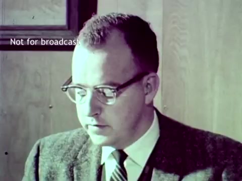 The still from 'IBM - The Information Center (1963)' features a man in glasses, focused on a task. He appears to be in an office environment, with wooden paneling in the background, indicative of the 1960s aesthetic. The image highlights the personal engagement with IBM's technology at the time, reflecting the use of computers and punch cards in educational contexts like grades and enrollment. The text 'Not for broadcast' suggests this is an archival piece intended for internal or educational use rather than public airing.