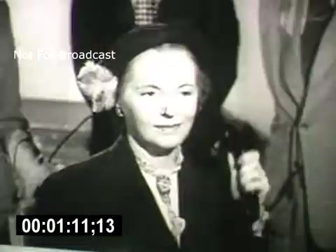 The still from 'Bell System - Story Without End' depicts a woman holding a telephone receiver, likely engaged in a conversation. She appears poised and attentive, suggesting the importance of communication in the narrative. The context relates to the impact of the Bell System on connectivity and personal interactions. The image captures a moment focused on human connection through technology.